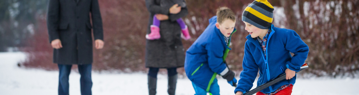 Young Family Playing Pond Hockey Outside In The Snow