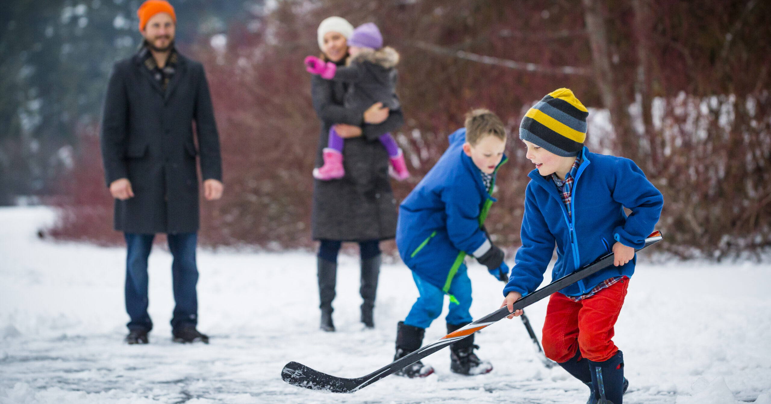 Young Family Playing Pond Hockey Outside In The Snow