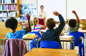 Education, Question With Group Of Children In Classroom And Raise Their Hands To Answer Learning Or Support, Diversity And Teacher Teaching With Young Students In Class Of School Building Together